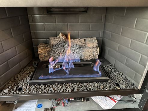 Gas fireplace with blue flames and artificial logs, surrounded by dark gray brick and rock.