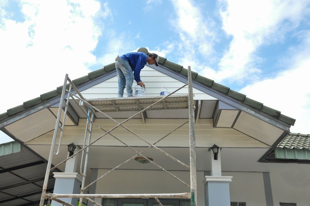 A man is painting the roof of a house on a scaffolding.