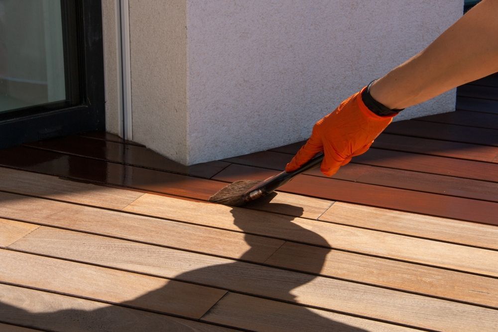 A person is painting a wooden deck with a brush.