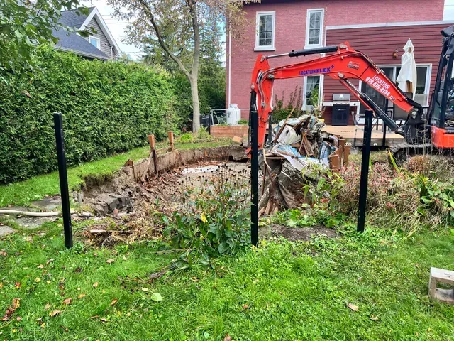 Une excavatrice creuse un trou dans l'arrière-cour d'une maison.