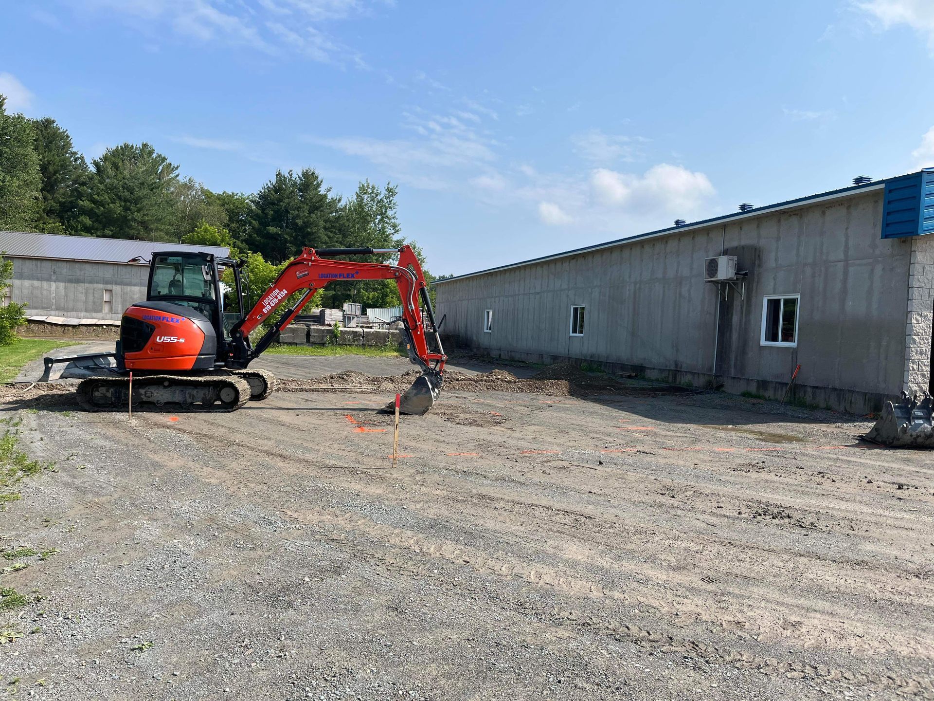 Une excavatrice est assise dans un terrain en gravier devant un bâtiment.