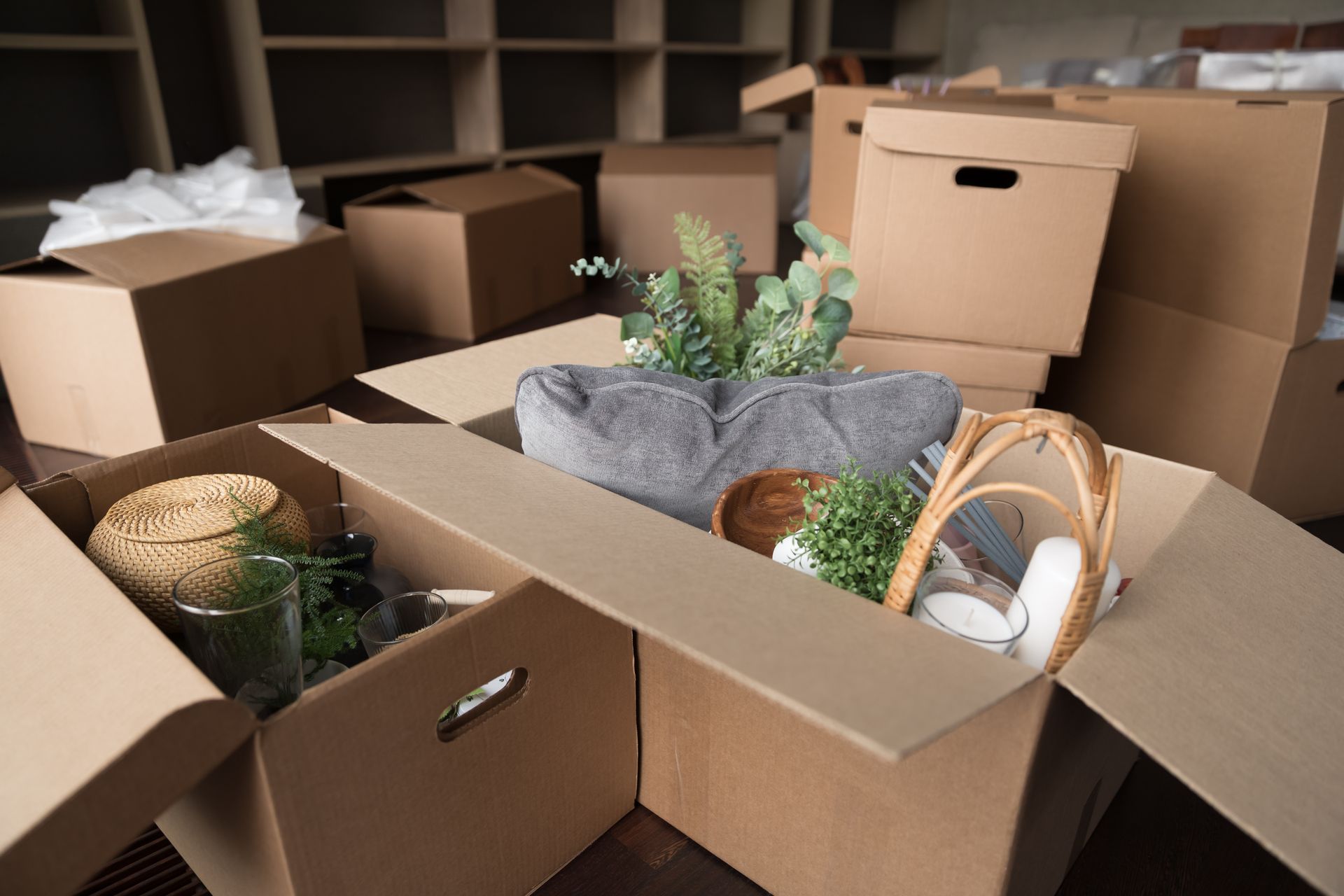 Cardboard boxes filled with items, likely during a move, in a room with empty shelves.