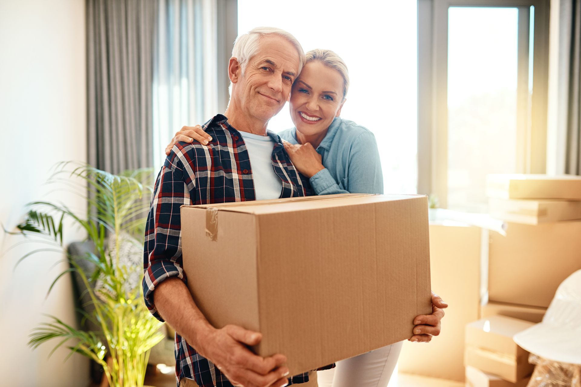 A man and a woman are holding a cardboard box in a living room.