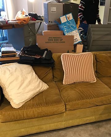 A mustard-yellow corduroy couch with pillows and stacks of boxes behind it, implying a move.