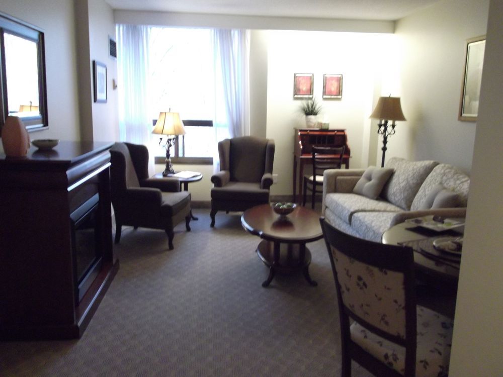 Living room with furniture, including a couch, chairs, lamps, and a coffee table, near a window.