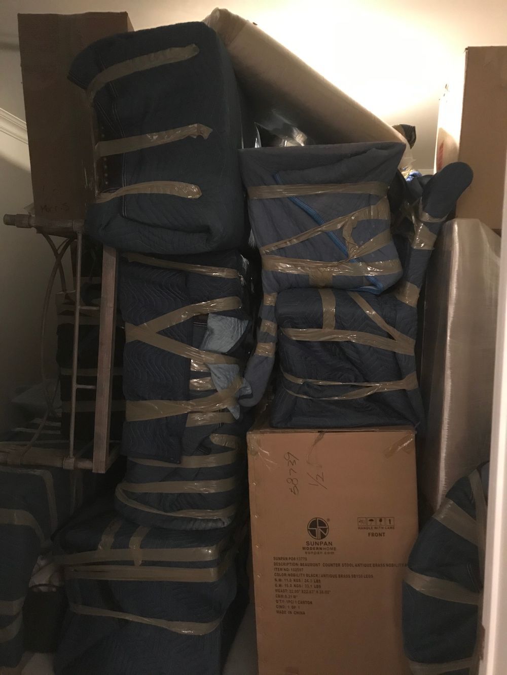 A packed storage space with wrapped furniture, boxes, and a tall rolled item.