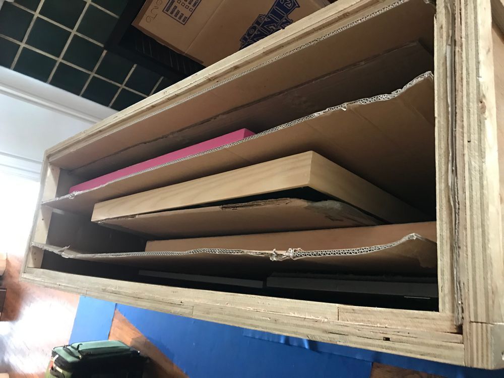 Wooden storage shelf with cardboard dividers holding flat art supplies.