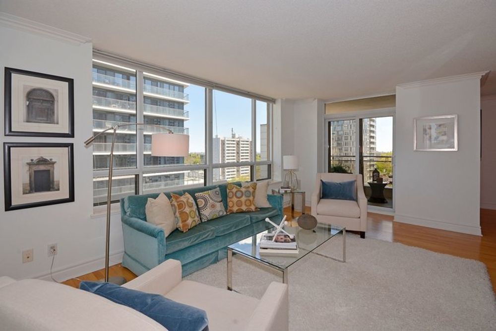 Living room with blue sofa, white chairs, glass coffee table, large windows, and city view.