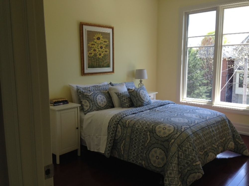 Bedroom with a bed, nightstand, window, and sunflower artwork on a yellow wall.