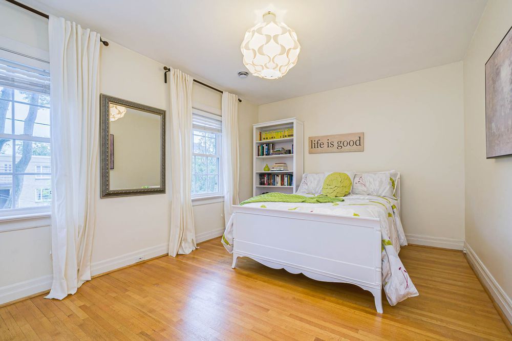 Bedroom with hardwood floors, white bed, large mirror, two windows, and patterned pendant light.