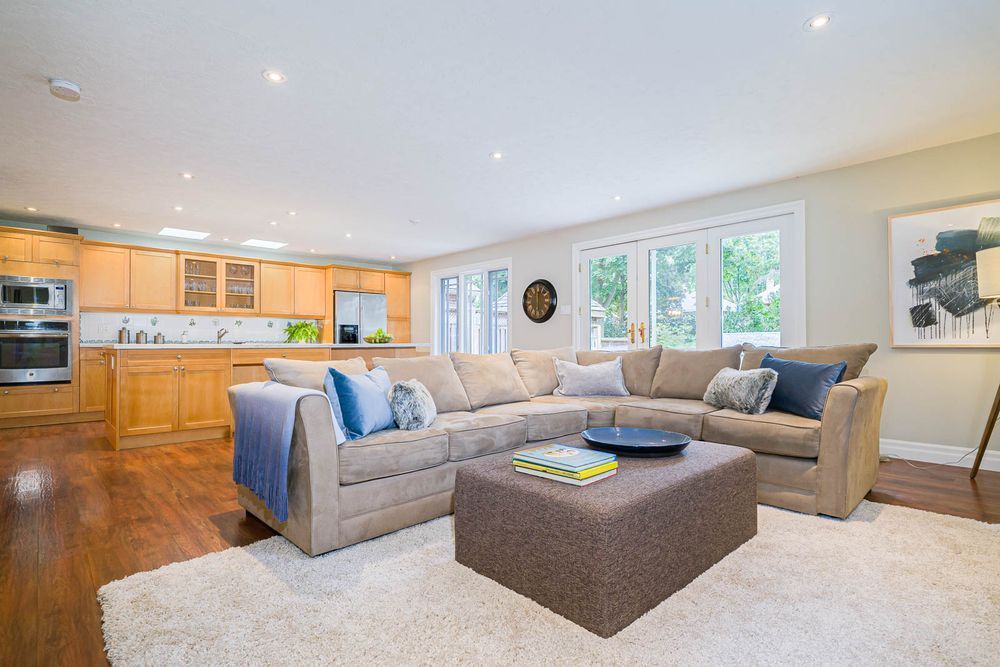 Open-concept living space with a beige sectional, wooden floors, and a kitchen with light wood cabinetry.