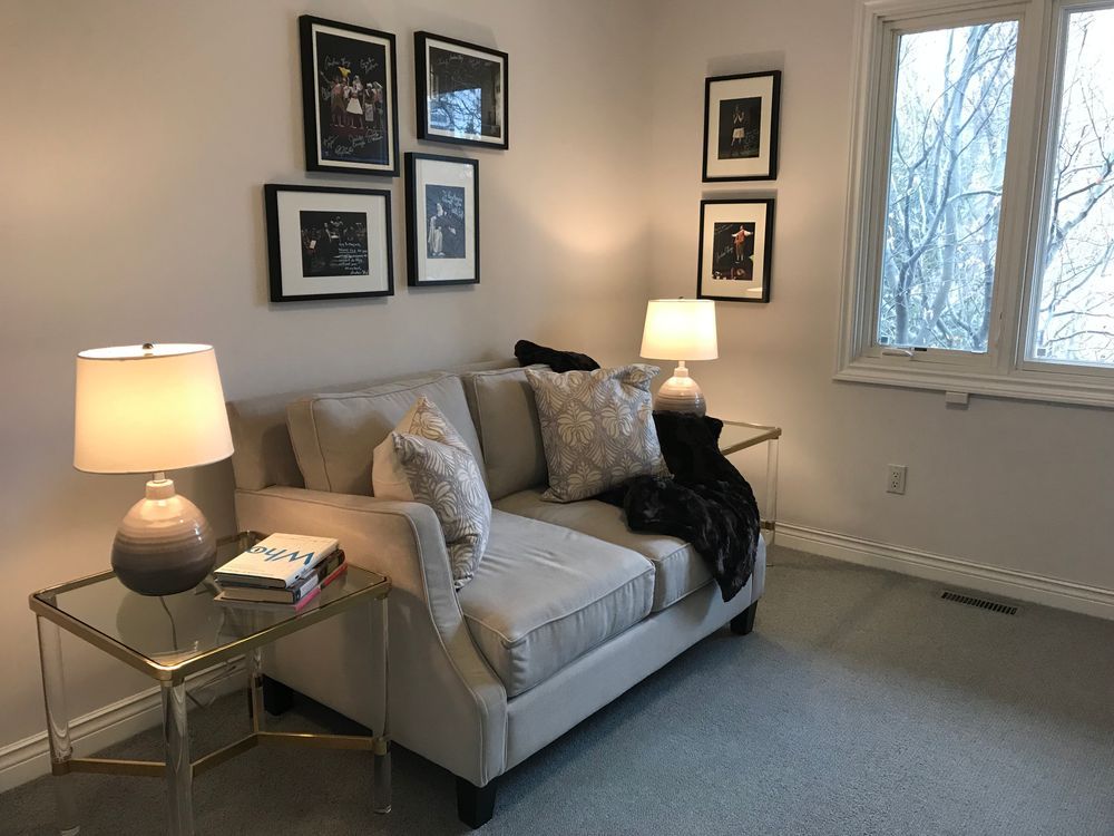 A small beige sofa sits between two glass-topped tables with lamps. Framed photos hang on the wall.