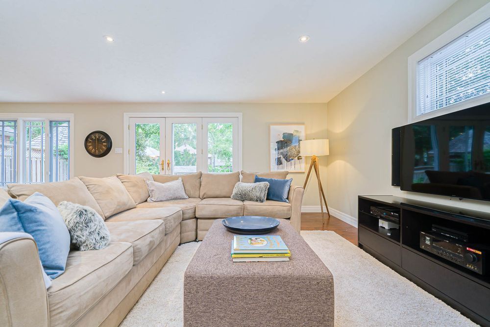 Cozy living room with a sectional sofa, ottoman, TV, and floor lamp. Beige walls and white trim.