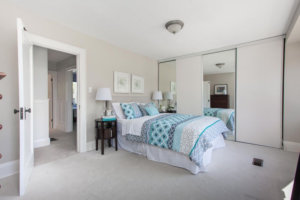Bedroom with bed, mirrored closet, and open doorway to hallway. Neutral color scheme.