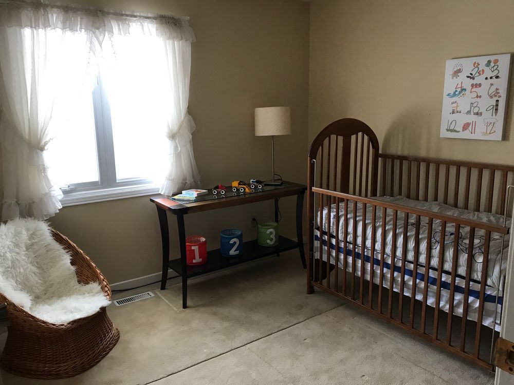 Baby's nursery with crib, wicker chair, console table, and window with sheer curtains.