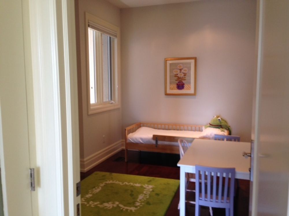A small child's room with a bed, desk, chair, and a green rug.