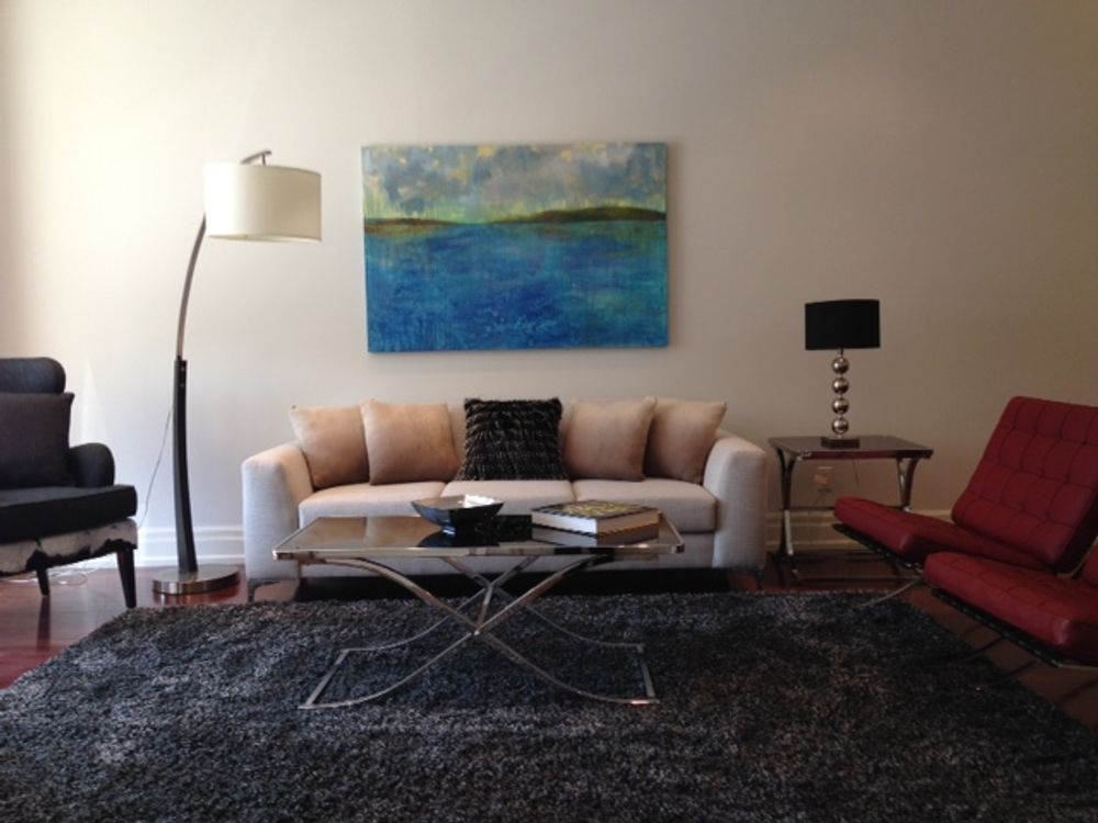 Living room with white sofa, blue artwork, two chairs, rug, and lamps.