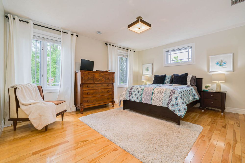 Bedroom with hardwood floors, a bed, dresser, chair, windows, and rug.
