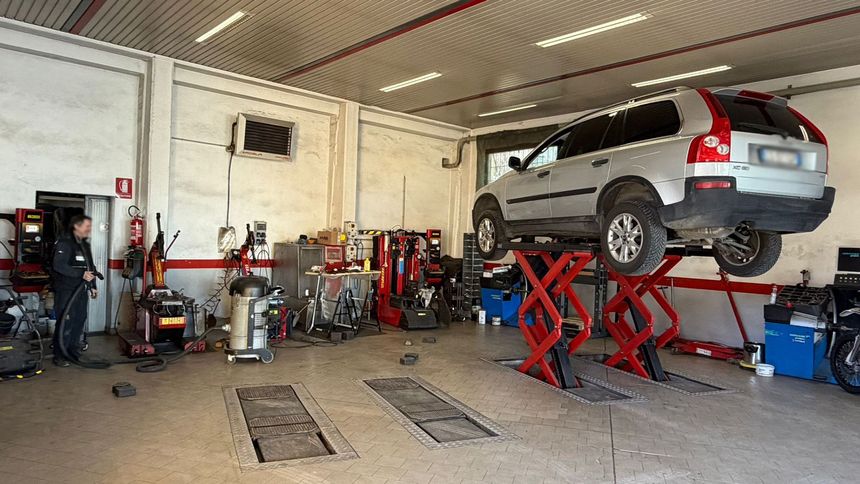 Un SUV Jaguar bianco sollevato su un ponte sollevatore idraulico a forbice rosso all'interno di un'officina meccanica.