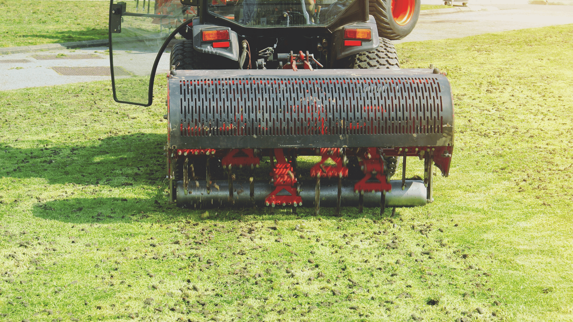 A tractor aerating a grassy lawn with a rotating spiked roller.