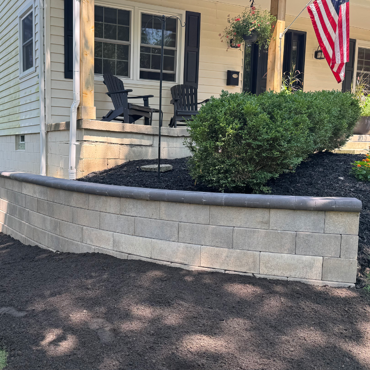Construction worker in yellow vest and hard hat placing a concrete block on a retaining wall outdoors.