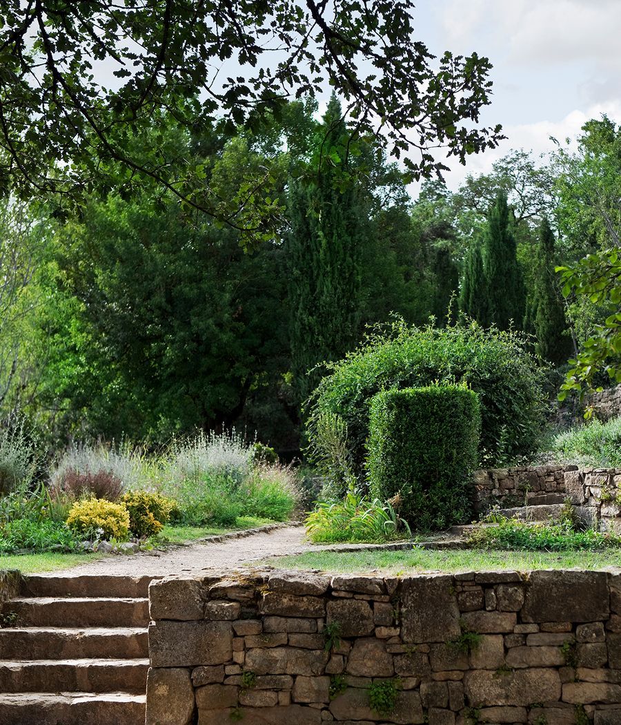 Stone steps lead to a garden path lined with lush greenery and a stone wall.