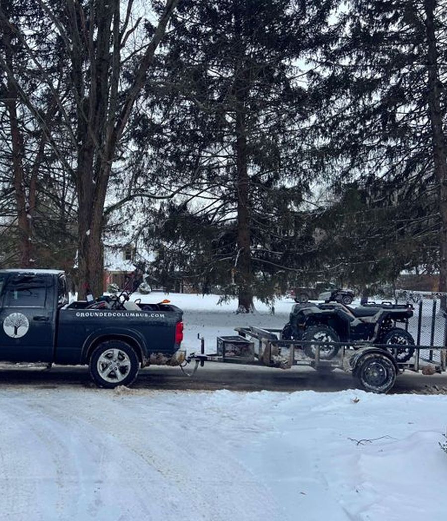 A truck is towing a four wheeler in the snow.