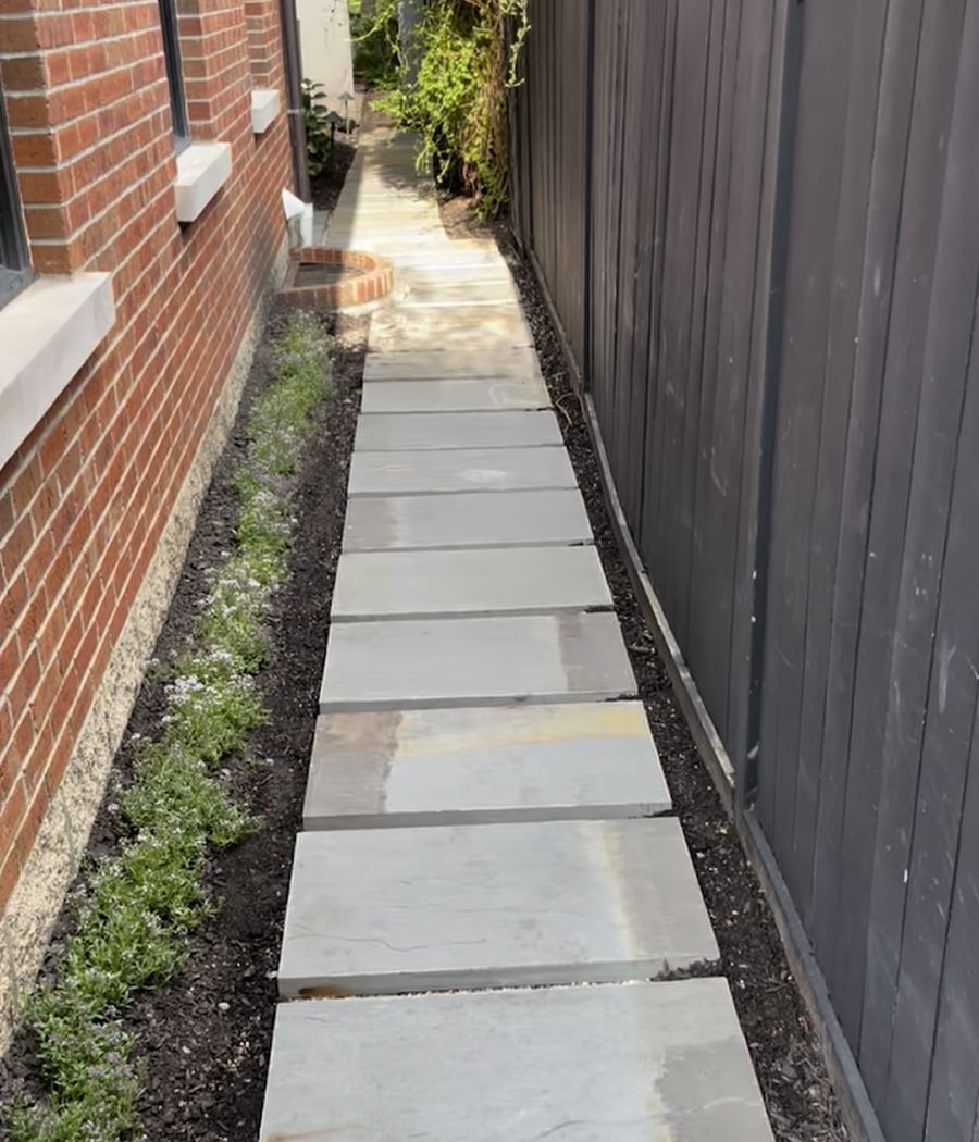 A stone walkway between a brick building and a wooden fence.
