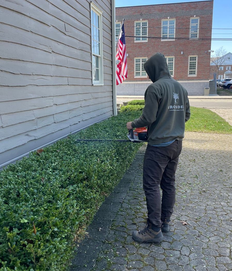 A man is cutting a bush with a chainsaw in front of a building