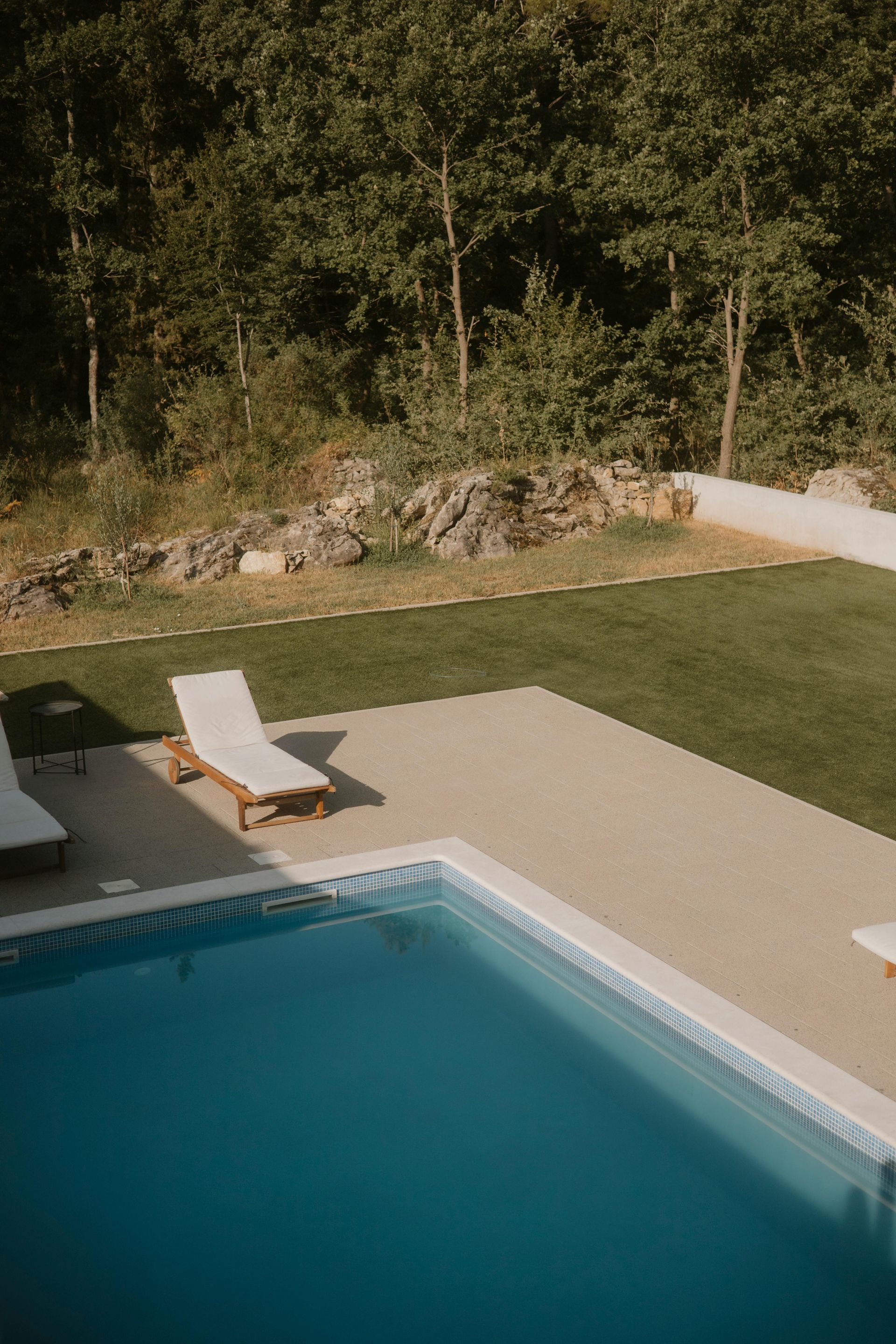 Outdoor patio with pool, lounge area, wooden pergola, and sliding glass doors to a modern house.