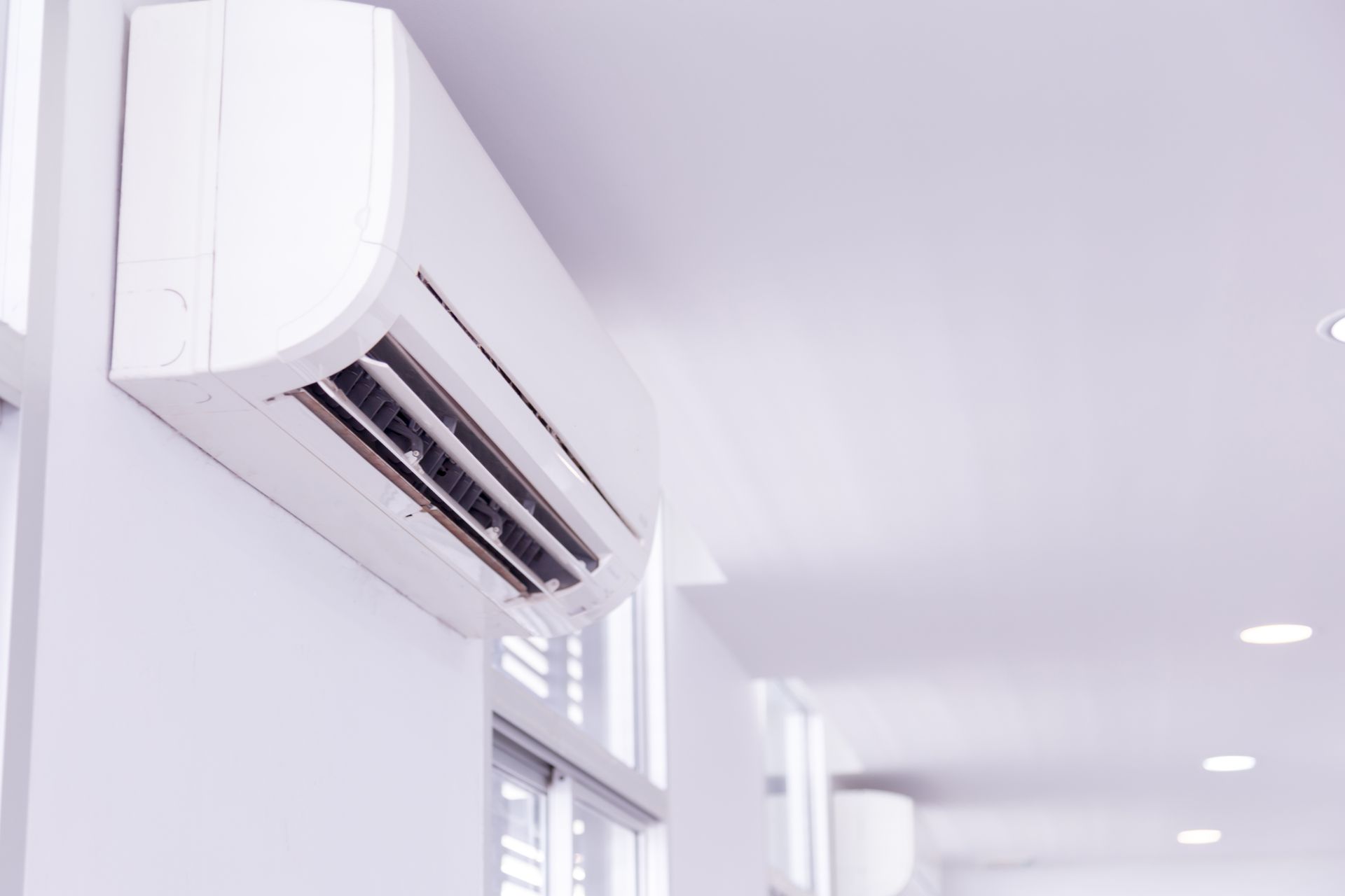 A white air conditioner is hanging on a white wall in a hallway.