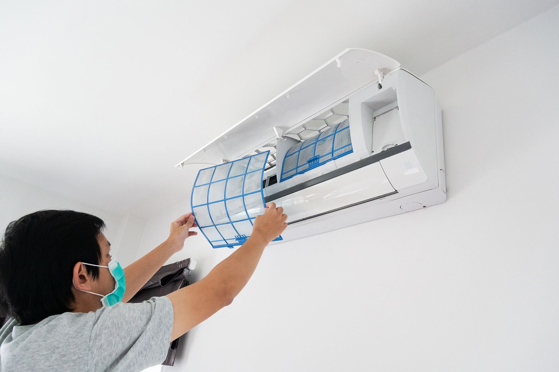 A man wearing a mask is cleaning an air conditioner.