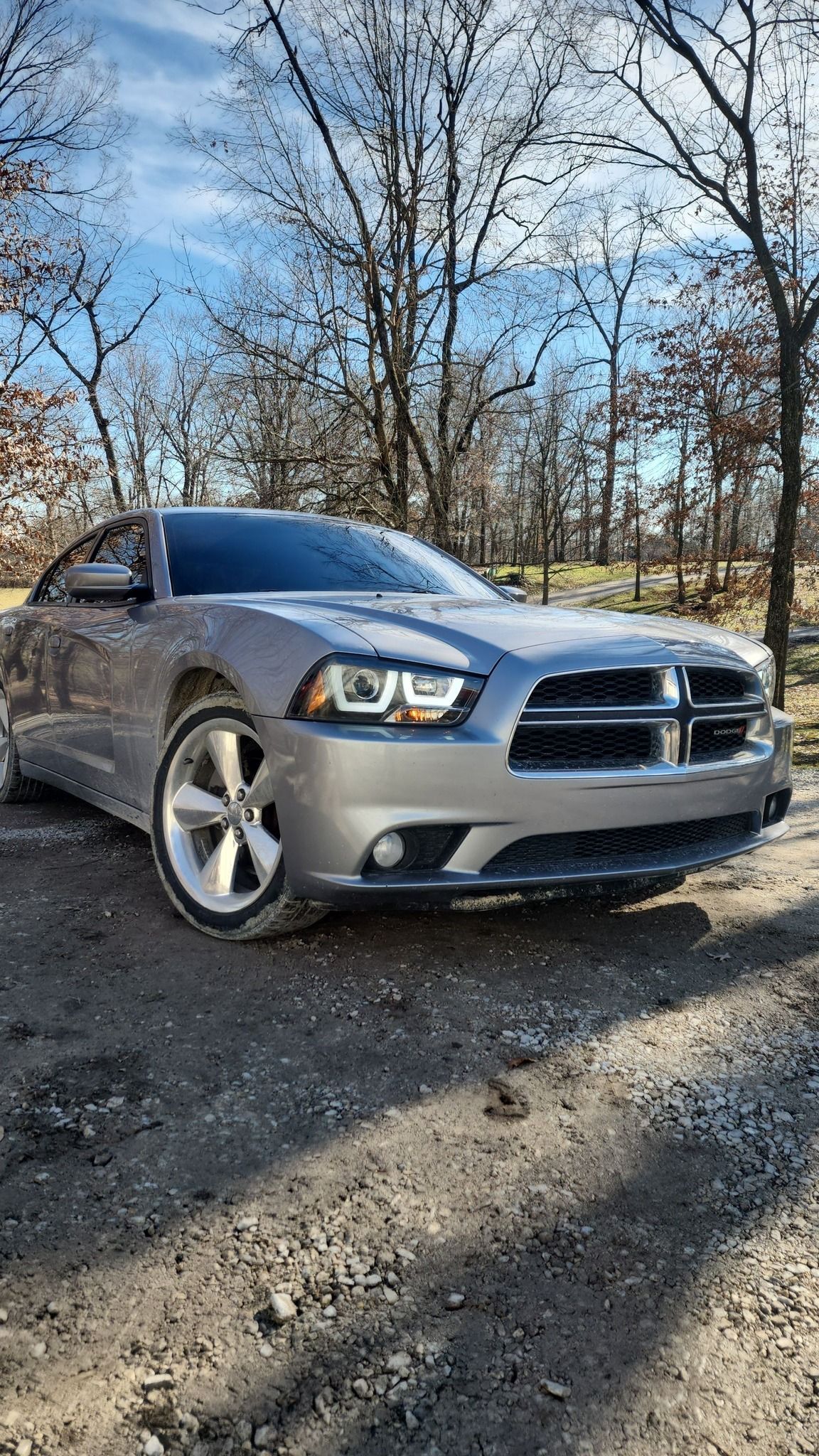 A silver dodge charger is parked on a dirt road.
