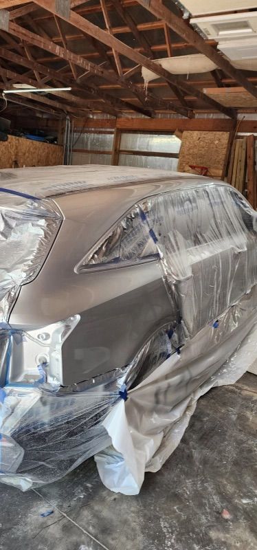 A car is covered in plastic while being painted in a garage.
