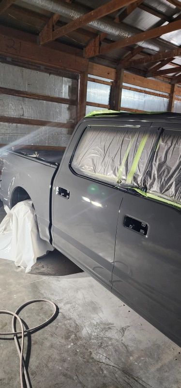 A gray truck is being painted in a garage.