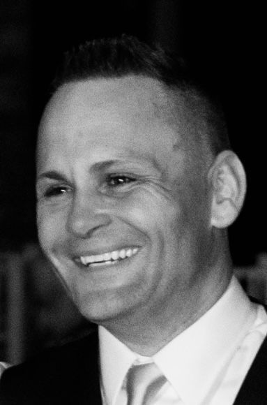 Man smiling, with a high-fade haircut, wearing a suit and tie.