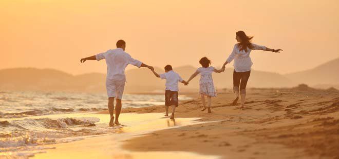 Family walking on a beach at sunset, holding hands with arms outstretched.