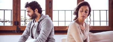 A man and a woman are sitting back to back on a couch.