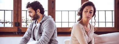 A man and a woman are sitting back to back on a couch.