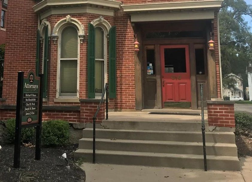 Red brick building with red door, steps leading up. Sign on the left.