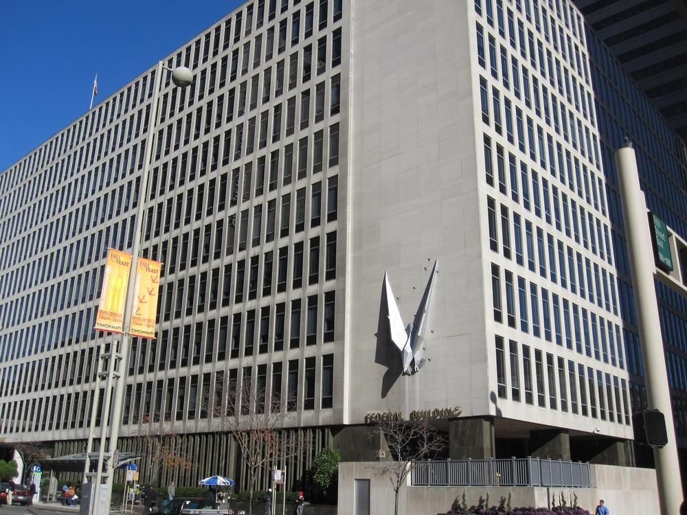 A tall concrete building with many rectangular windows and a large clock sculpture on its side.