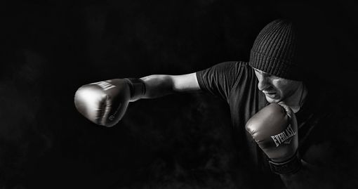 Boxer throwing a punch, wearing gloves and a beanie, in a dark setting.