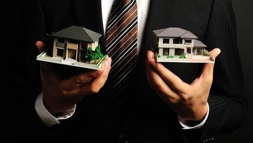 Man in suit holding two miniature houses, likely real estate presentation.
