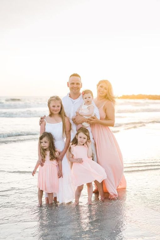 Family of seven at the beach. Adults, children standing in the water. Sunlight, soft colors.