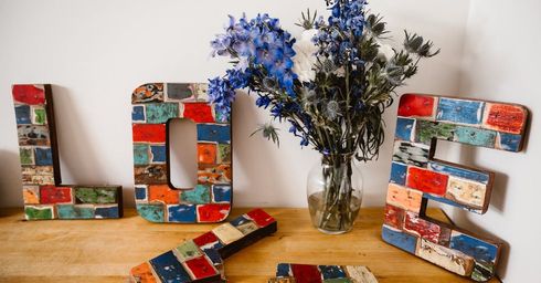 A wooden sign that says `` love '' is sitting on a wooden table next to a vase of flowers.