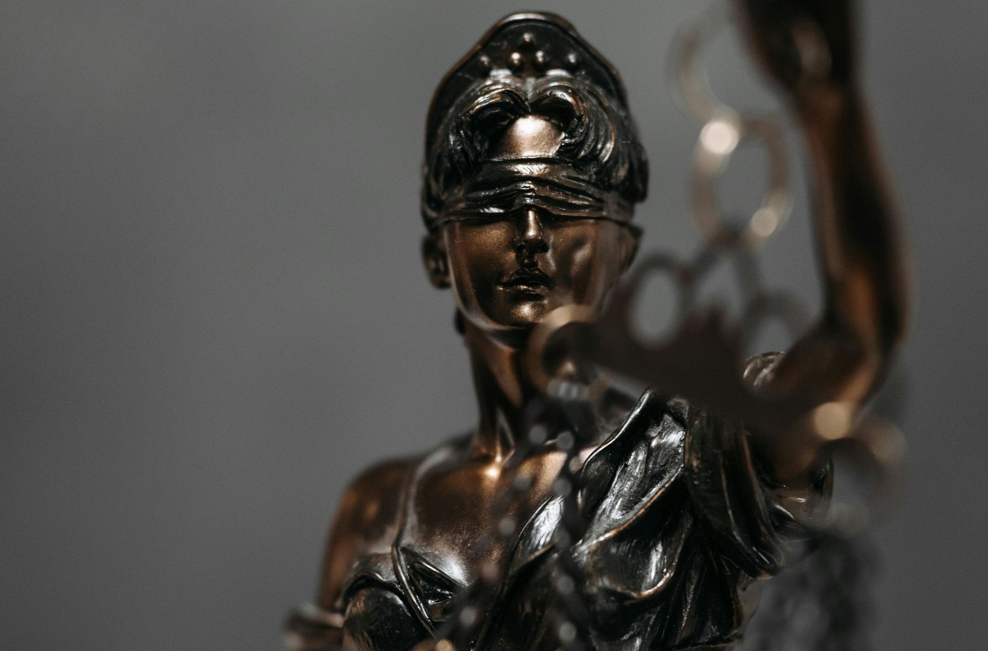 Statue of Lady Justice, blindfolded, holding scales. Bronze color, blurred background.