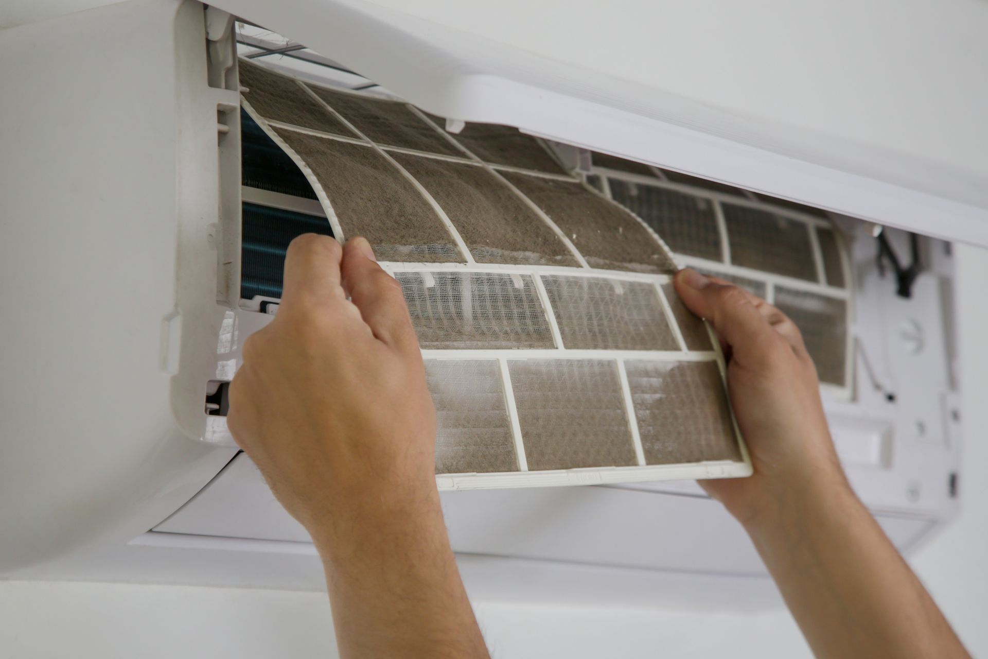 Closeup of a man holding a dirty AC filter as he takes it out of the system.