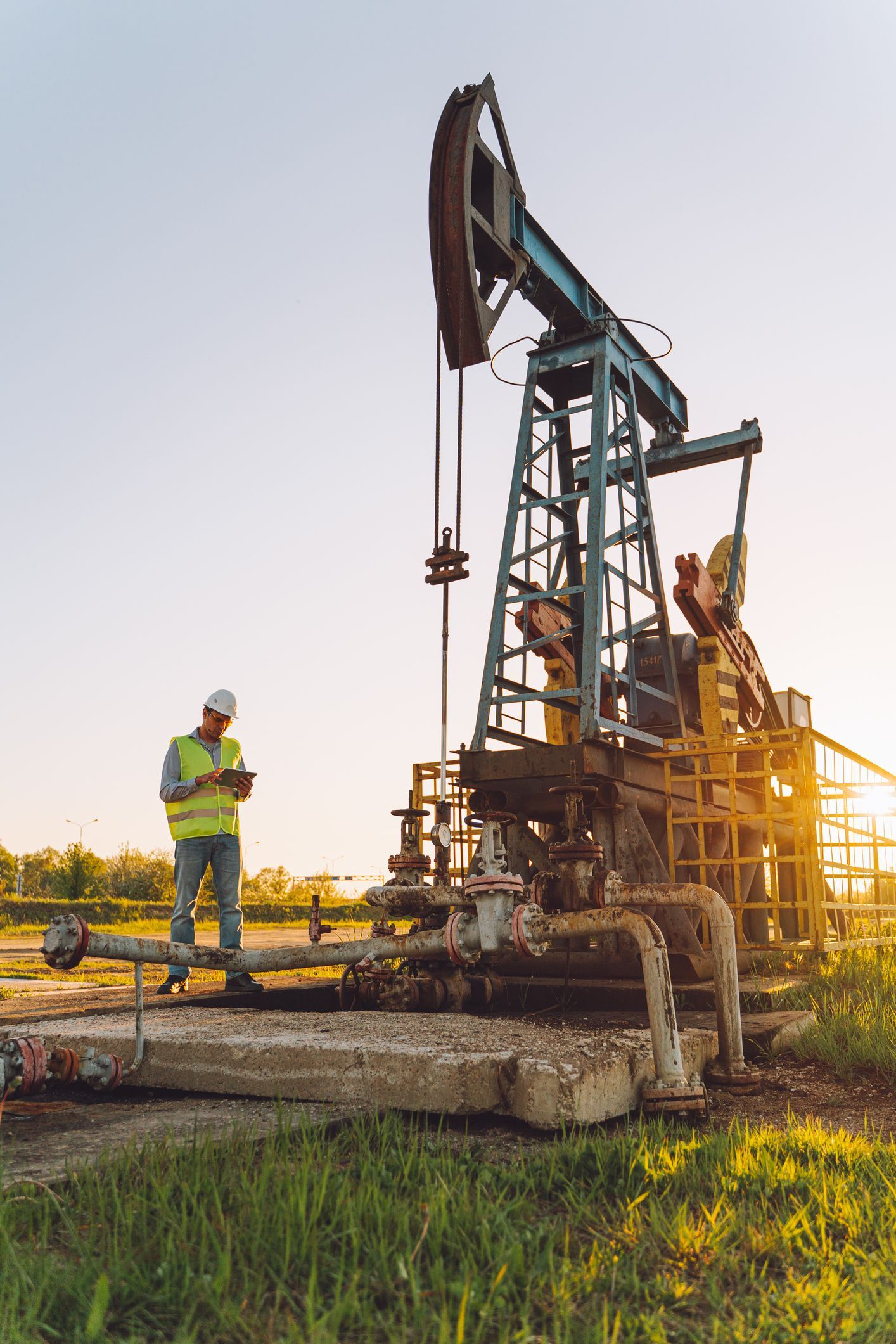 Manager in helmet and protective glasses analyzing data on oil well field.