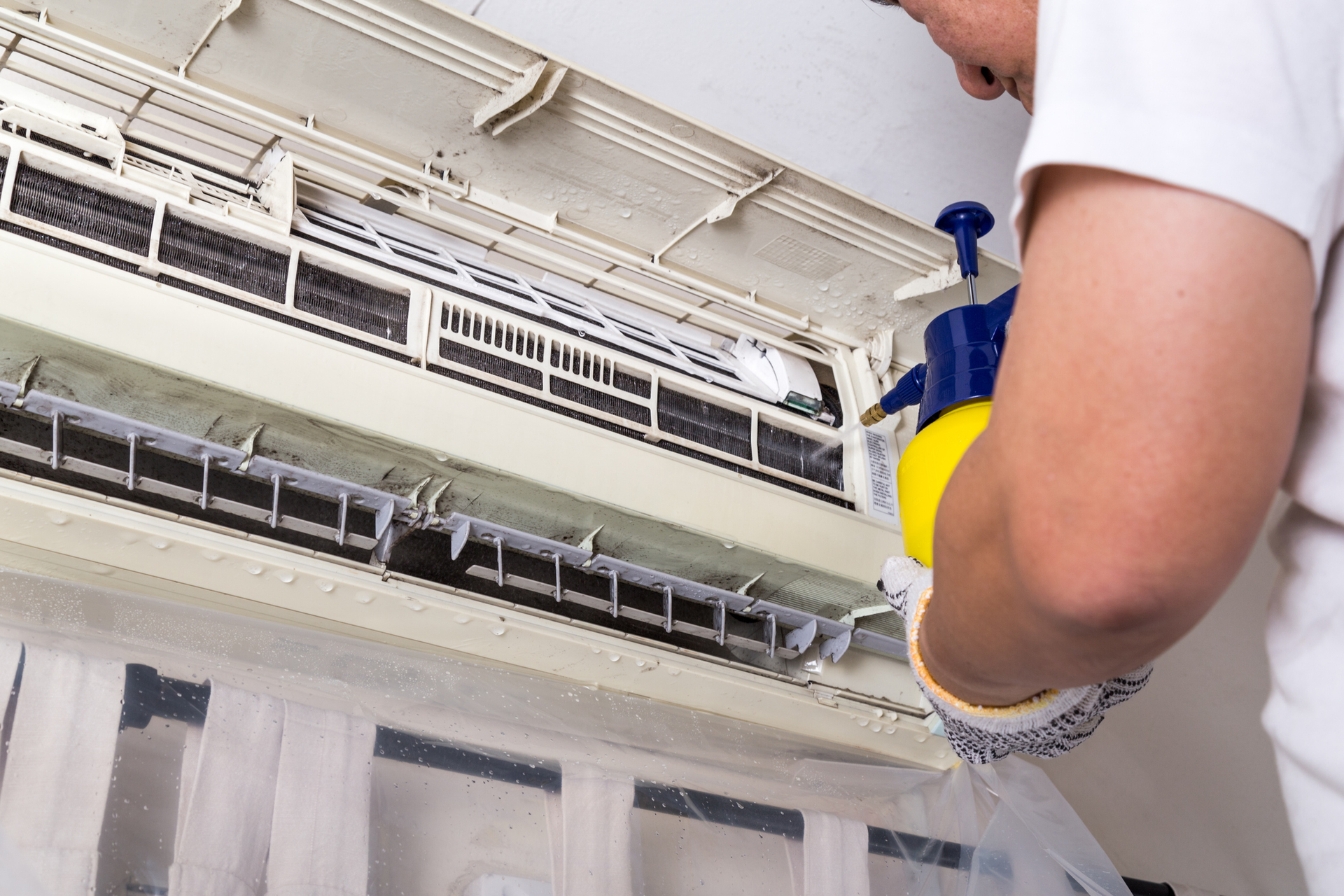 Male technician sprays an AC with a liquid solution.