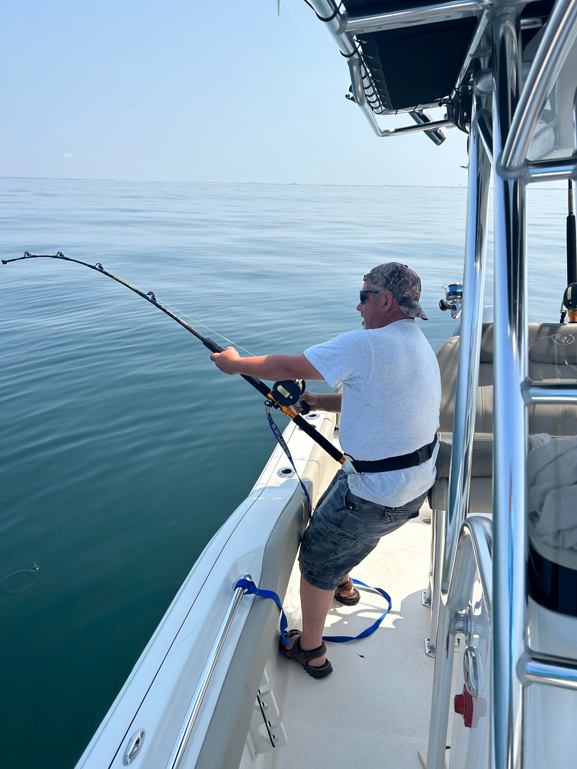 Man fishing on a boat, holding a bent fishing rod, over water.